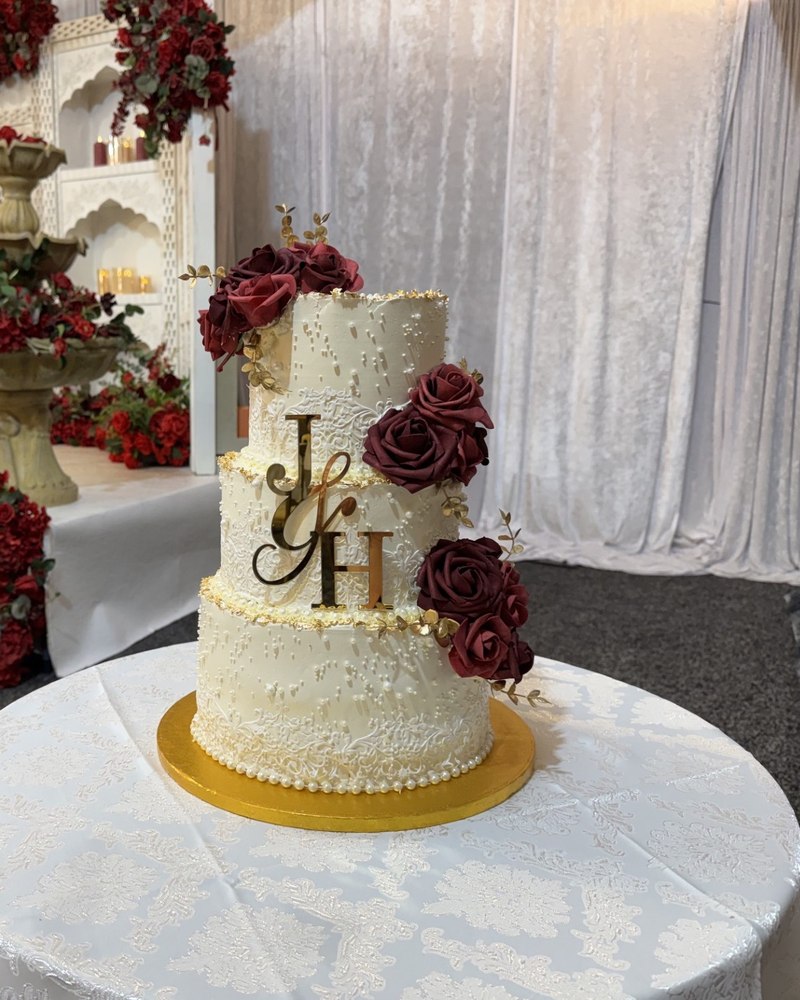 Three-tier ivory wedding cake with lace detail and burgundy rose cascade, J&H monogram