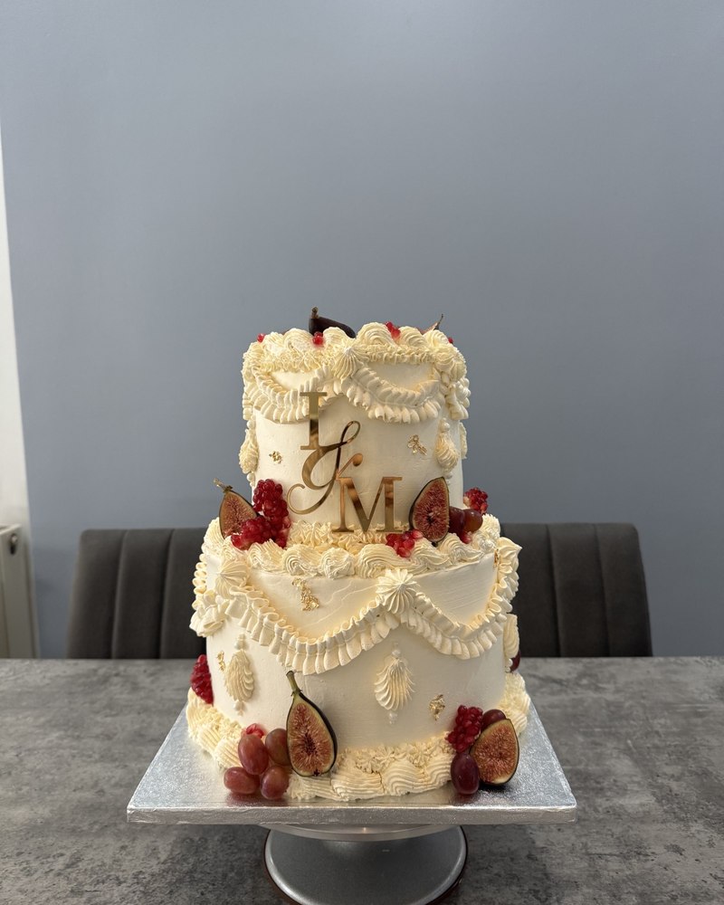 Two-tier wedding cake with piped drapes, fresh figs, pomegranate and grapes, I&M monogram